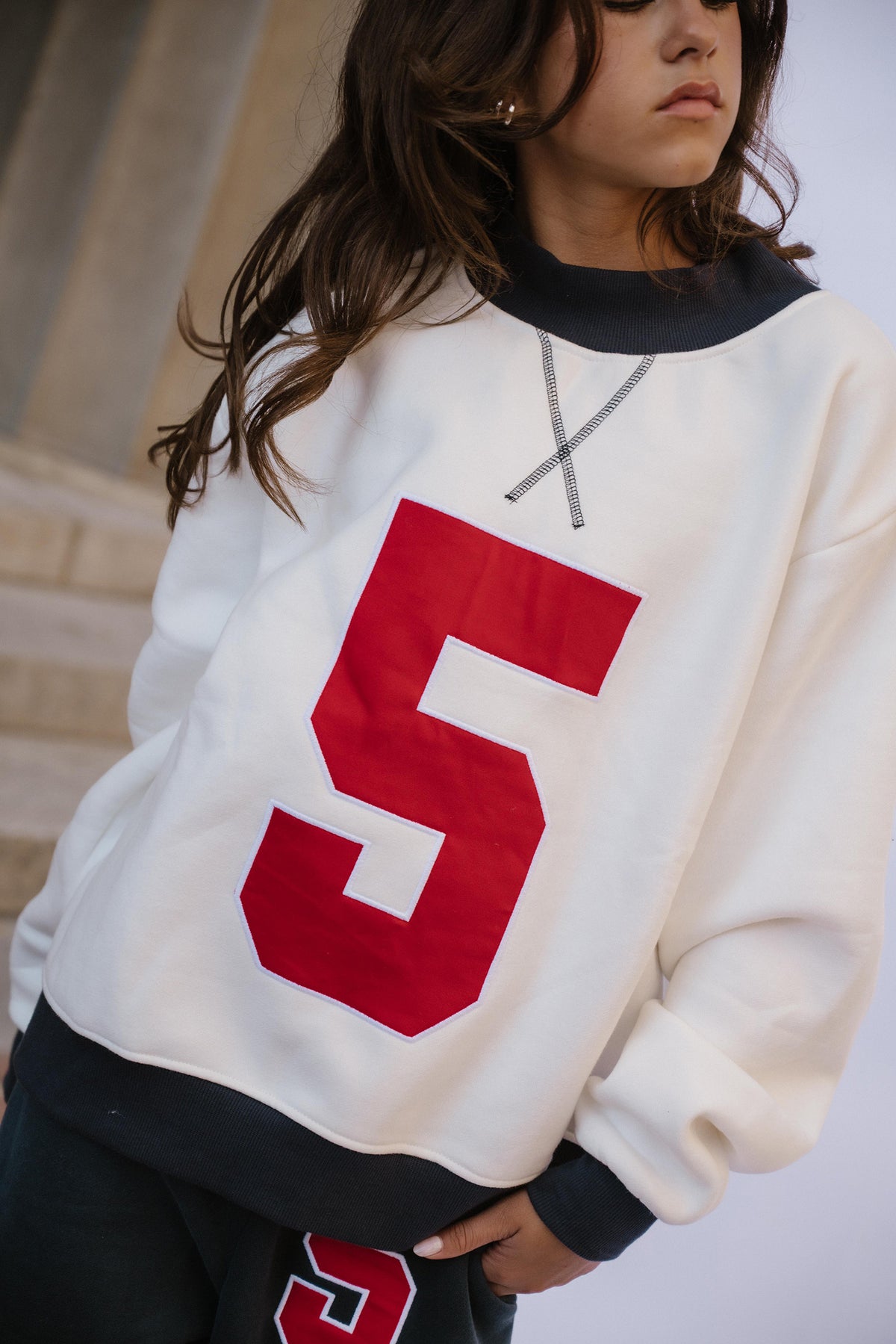 kids, A close-up of a girl wearing an oversized white sweatshirt with a large red number 5 on the front, a navy ribbed collar and cuffs.