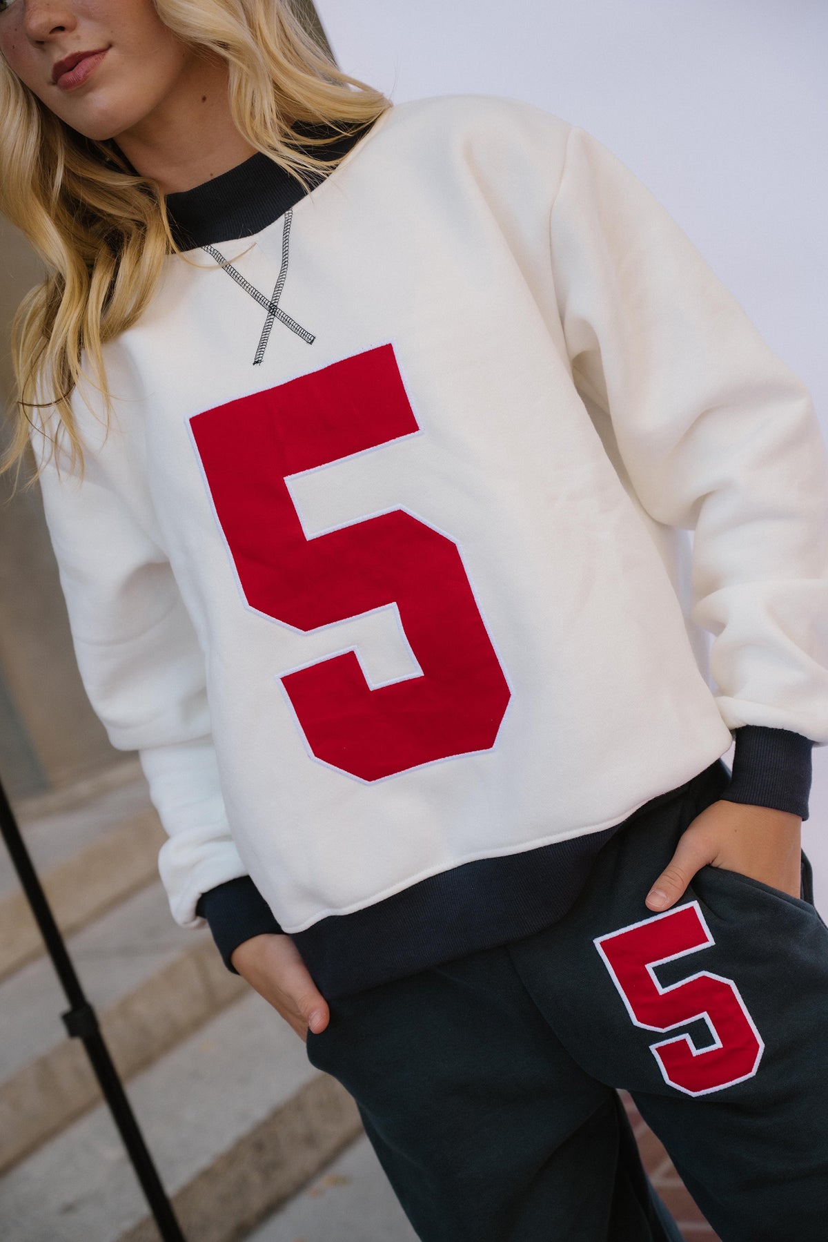 teen, A teen wearing a cream-colored crewneck sweatshirt with a large red number 5 on the front, paired with dark navy sweatpants that also feature a red and white number 5 on the thigh.