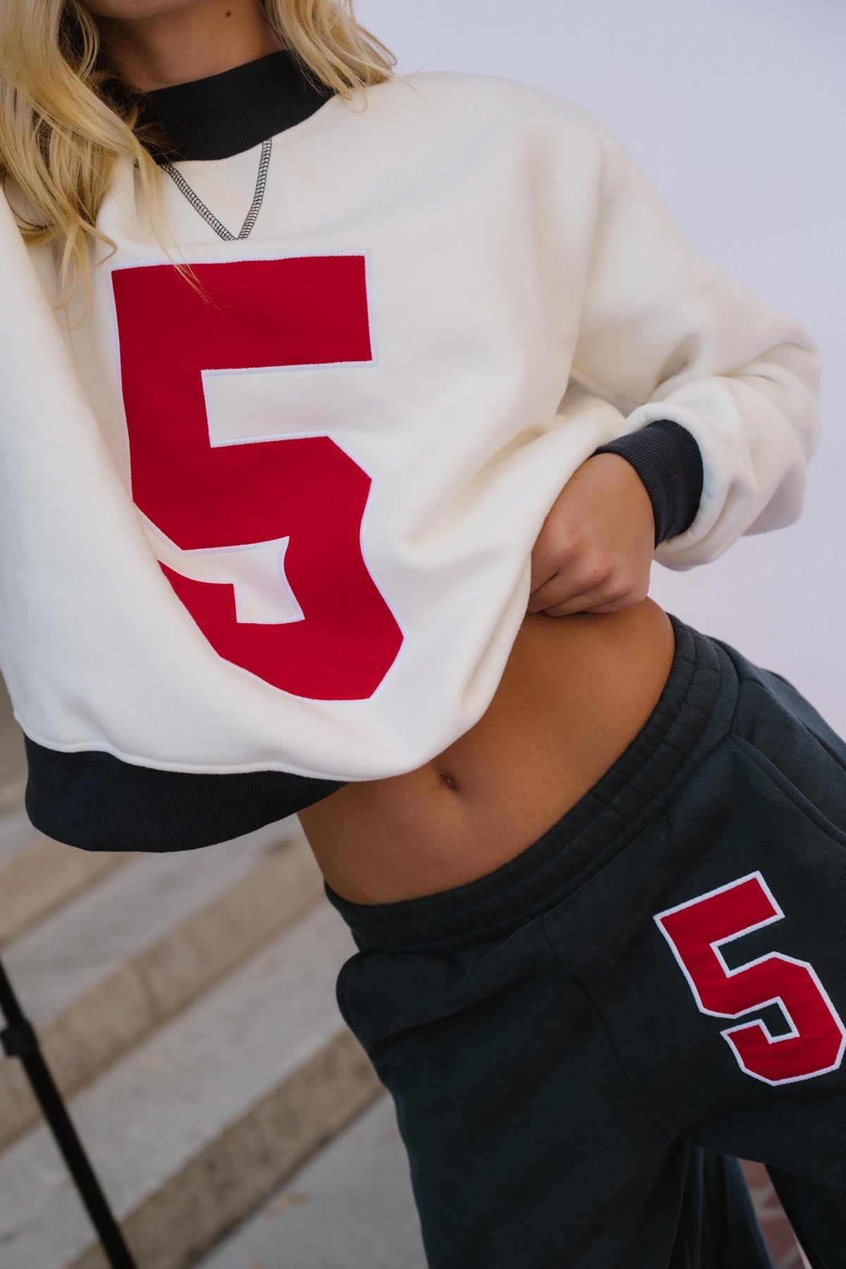 teen, A close-up of a girl wearing a cream sweatshirt with a large red number 5 on the front, paired with dark navy sweatpants featuring a matching red number 5 on the thigh.