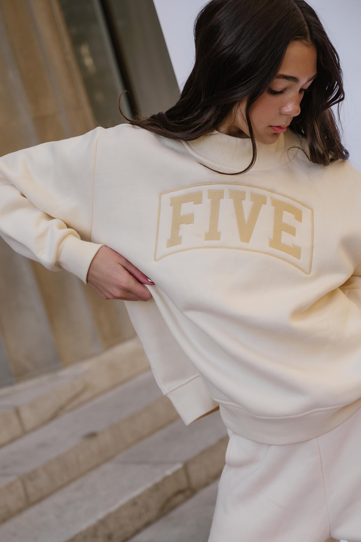 kids, A girl wearing a butter-yellow colored sweatshirt with 'FIVE' arched in a lighter beige color across the chest, standing on stone steps.