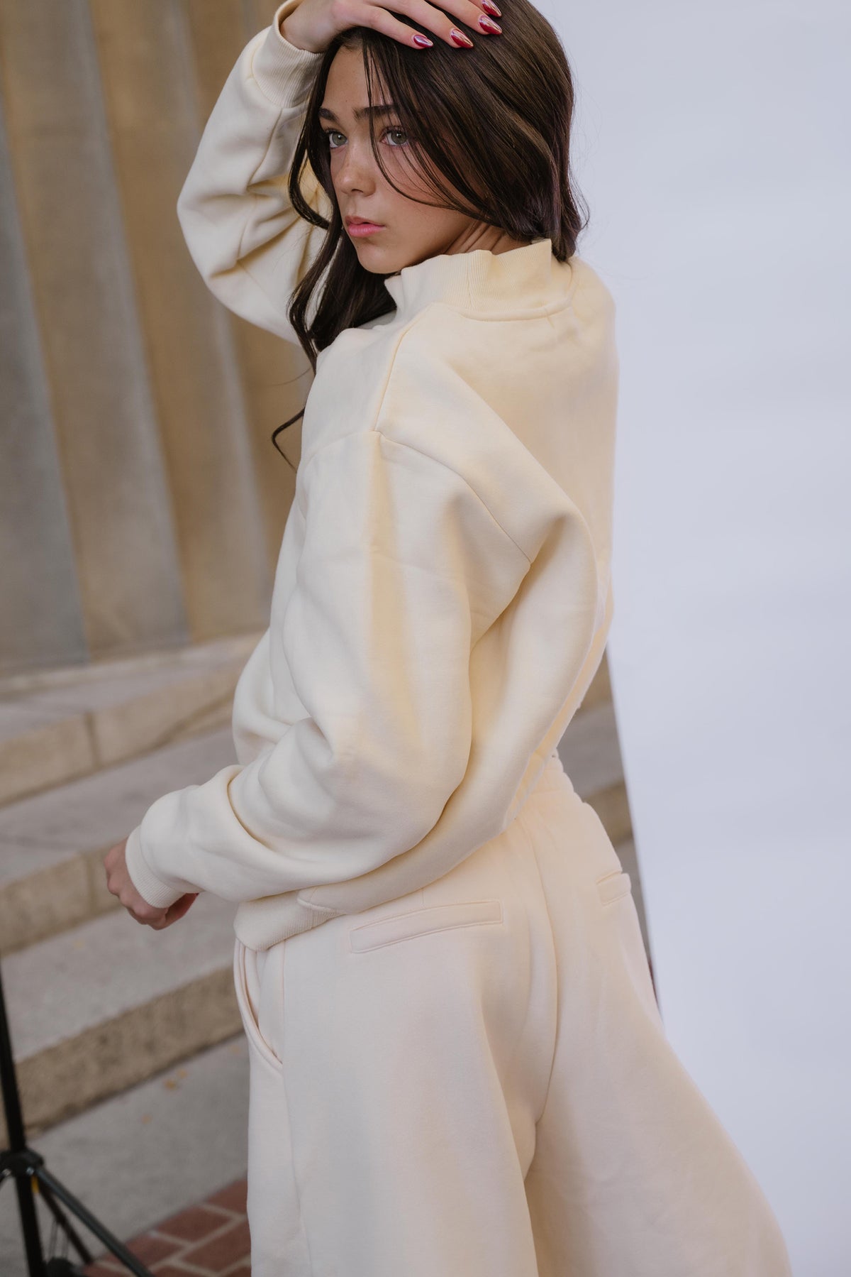 kids, A girl wearing a butter yellow-colored high-neck sweatshirt and matching sweatpants, photographed in a studio setting with a light gray backdrop and stone steps in the background.