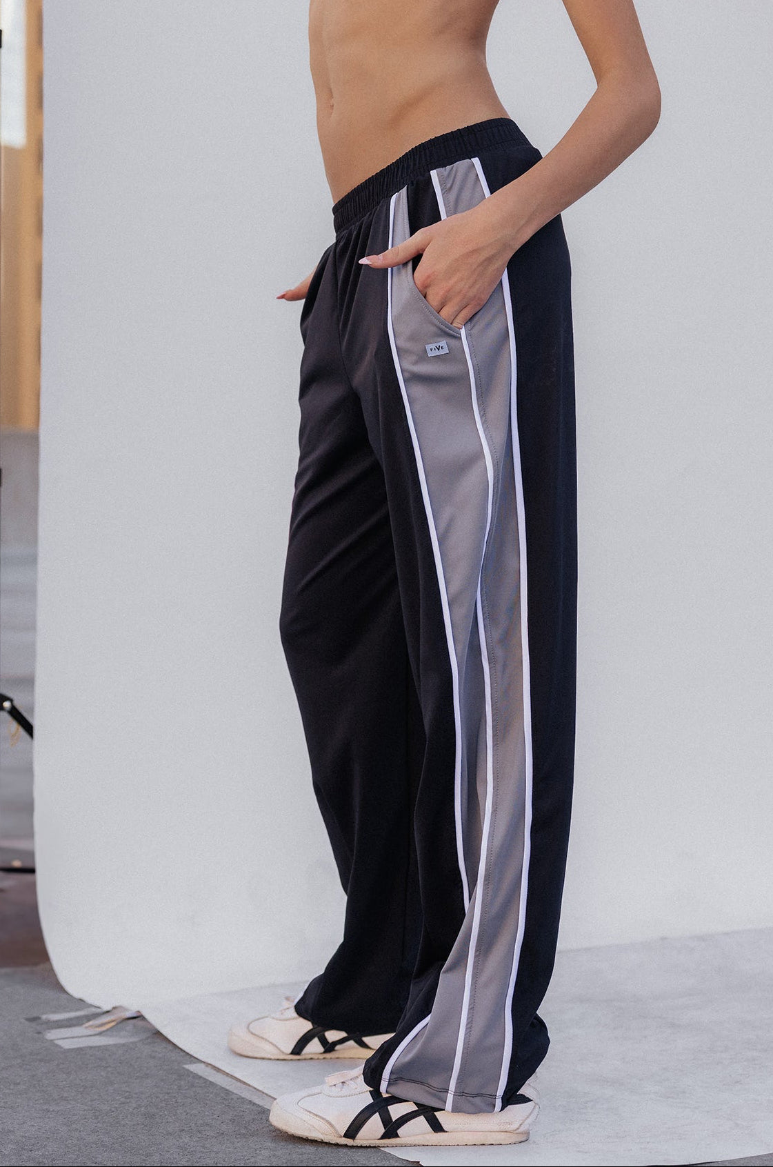 kids, A girl modeling black athletic pants with a sheer white side stripe, paired with a black sports bra, standing in front of a white studio backdrop.