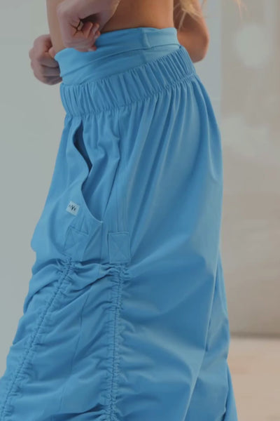 kids, A model wearing bright blue ruched ruched sweatpants, styled with a matching blue sports bra and white sneakers, standing on a white platform.