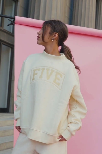 kids, A girl wearing a butter-yellow colored sweatshirt with 'FIVE' arched in a lighter beige color across the chest, standing on stone steps.