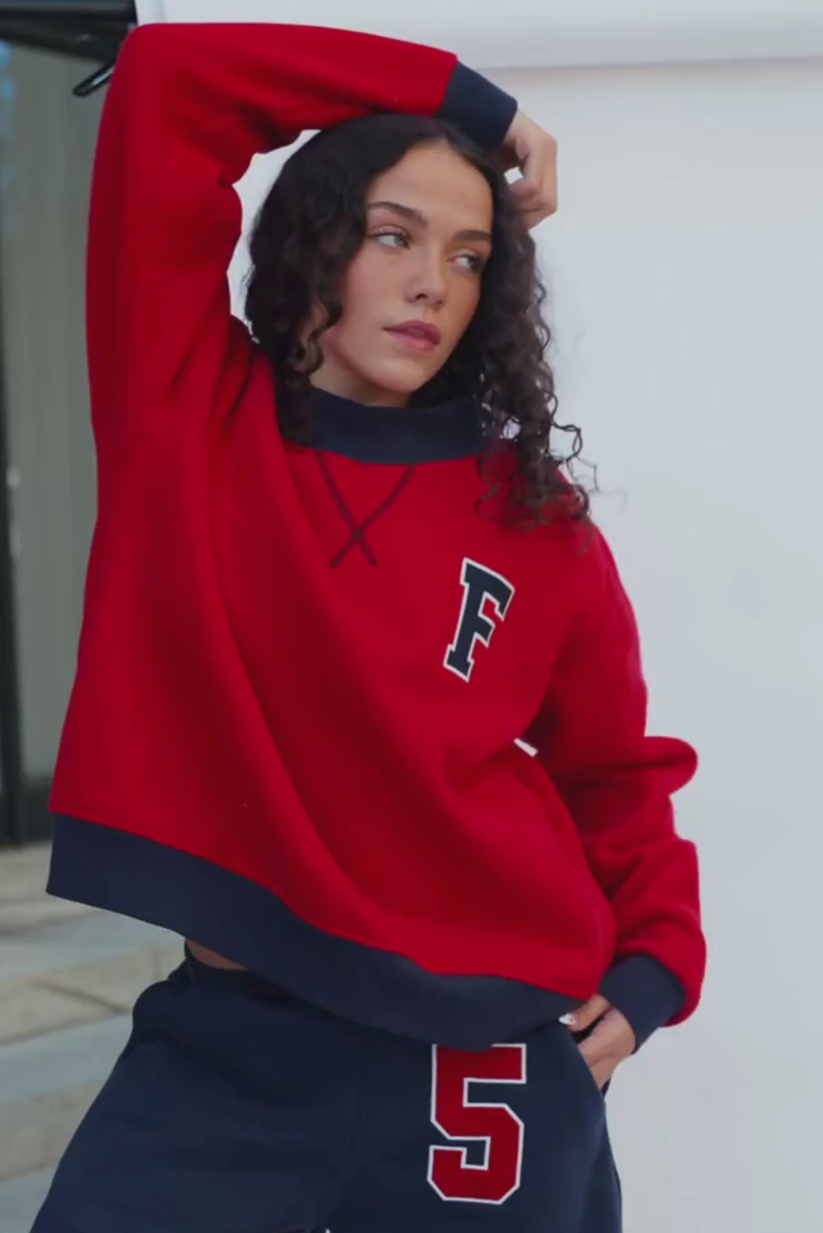teen, A girl wearing a red sweatshirt with a navy collar and a large letter 'F' on the chest, paired with navy pants featuring a red and white number '5'.