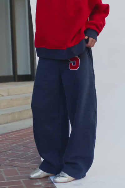 kids, navy wide-leg sweatpants with a red and white number 5 on the upper left thigh, modeled outdoors on a white surface with brick steps in the background.