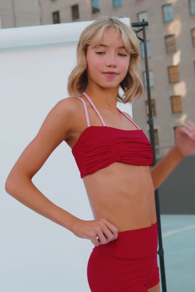 teen, teen wearing a bright red ruched sports bra with light pink straps, paired with matching red bottoms, photographed in an outdoor urban setting.