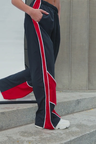kids, a video of a Black wide-leg sweatpants with bold red and white side stripes, worn by a model standing on concrete steps.