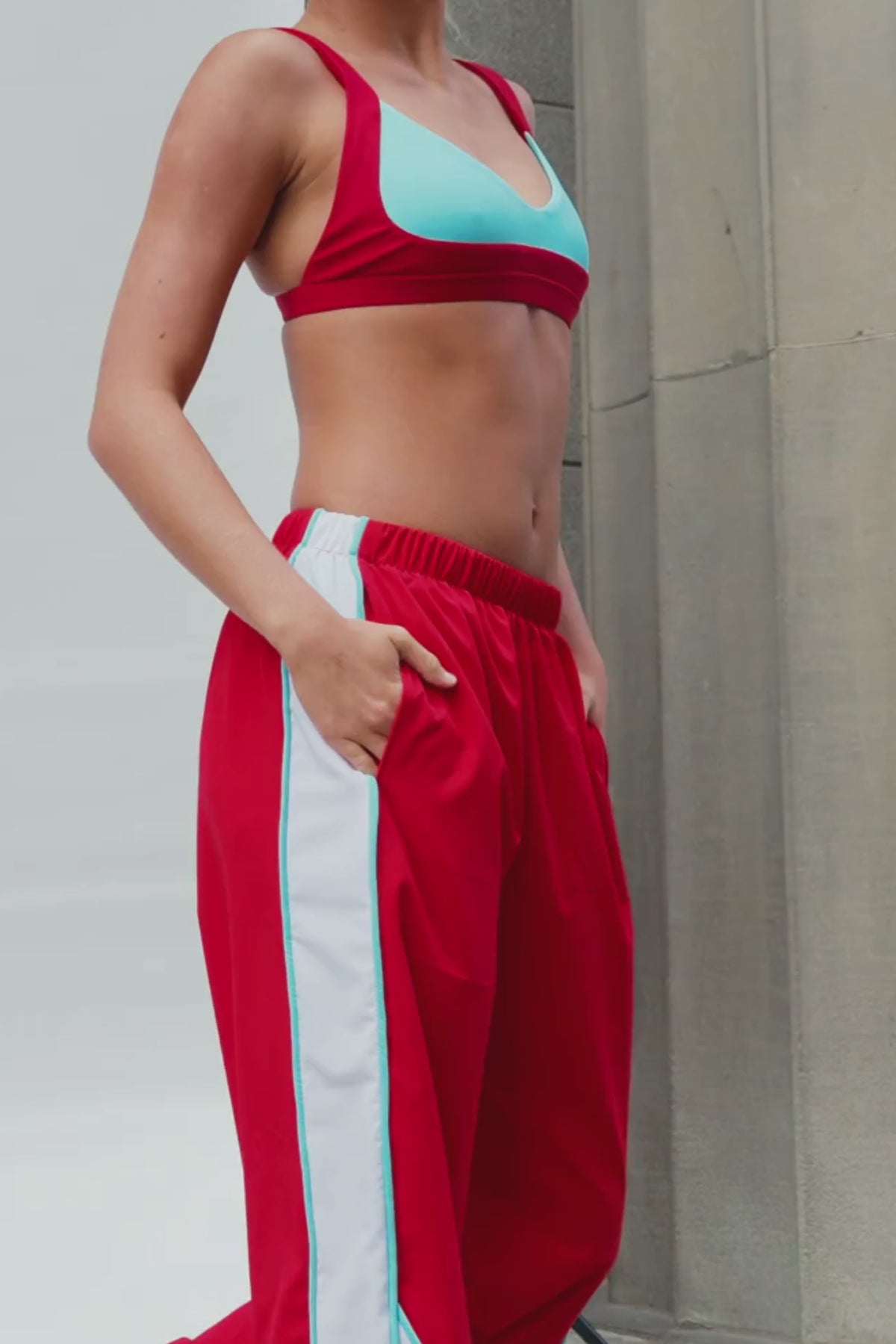 teen, A person wearing red wide-leg track pants with bold white side panels and mint green piping, standing on stone steps.