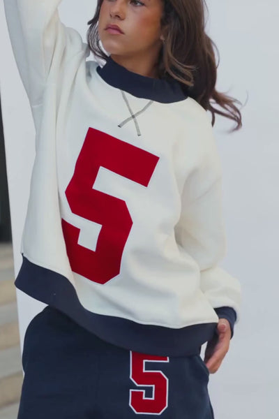 kids, A close-up of a girl wearing an oversized white sweatshirt with a large red number 5 on the front, a navy ribbed collar and cuffs.