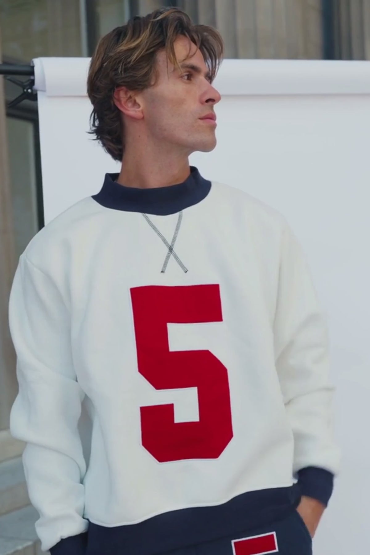 mens, A man wearing a cream-colored long-sleeve sweatshirt with a large red number 5 on the front, paired with dark navy pants featuring a matching red and white number 5 on the thigh.