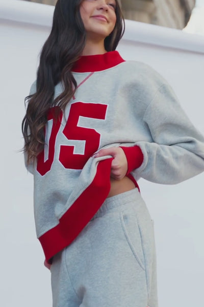kids, A girl modeling a light gray and red two-piece sweatshirt and sweatpants set, standing outdoors against a white wall.