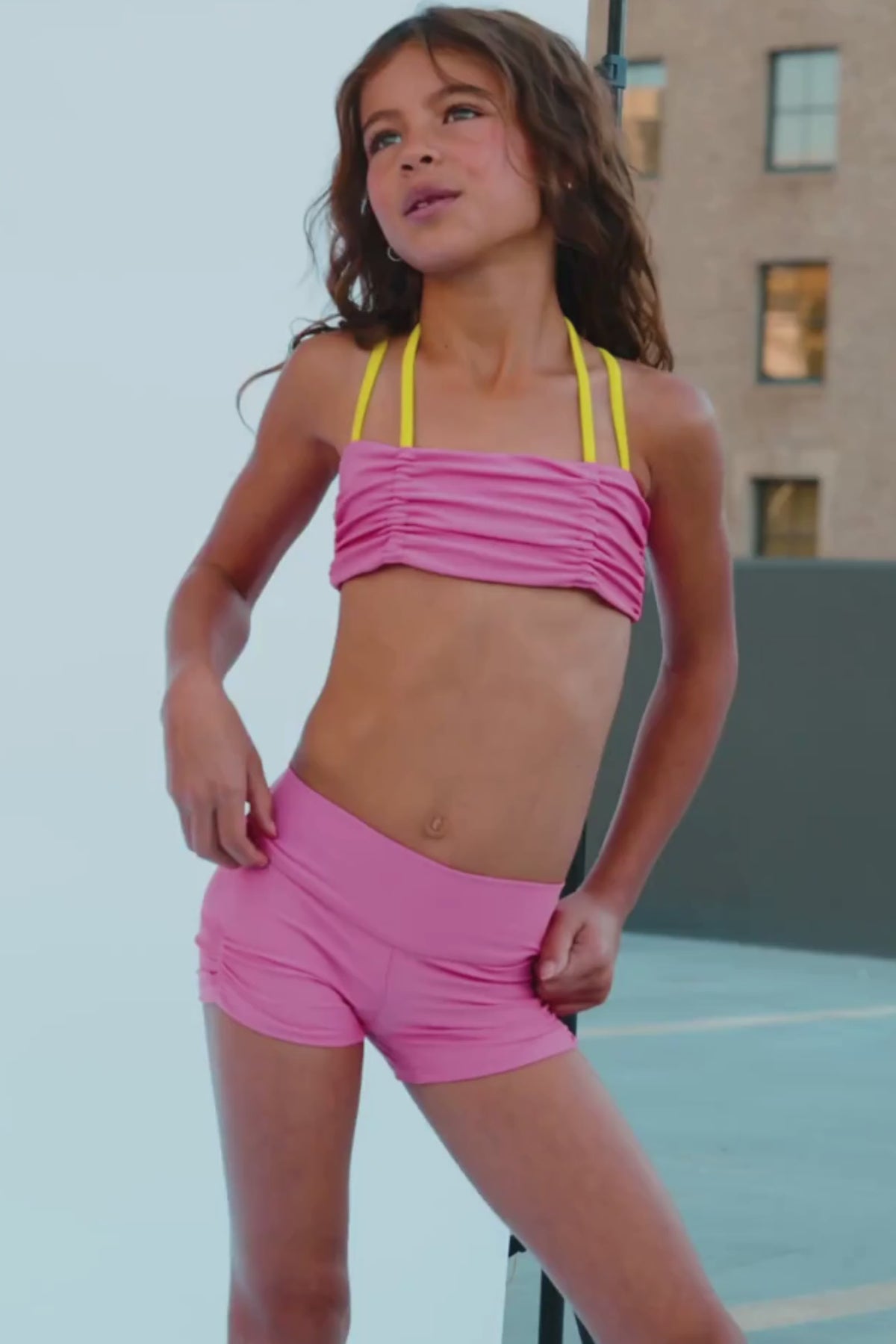 kids, A person wearing bright pink athletic shorts, white socks, and white sneakers, standing outdoors on a gray surface.