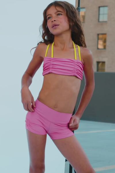 kids, A person wearing bright pink athletic shorts, white socks, and white sneakers, standing outdoors on a gray surface.