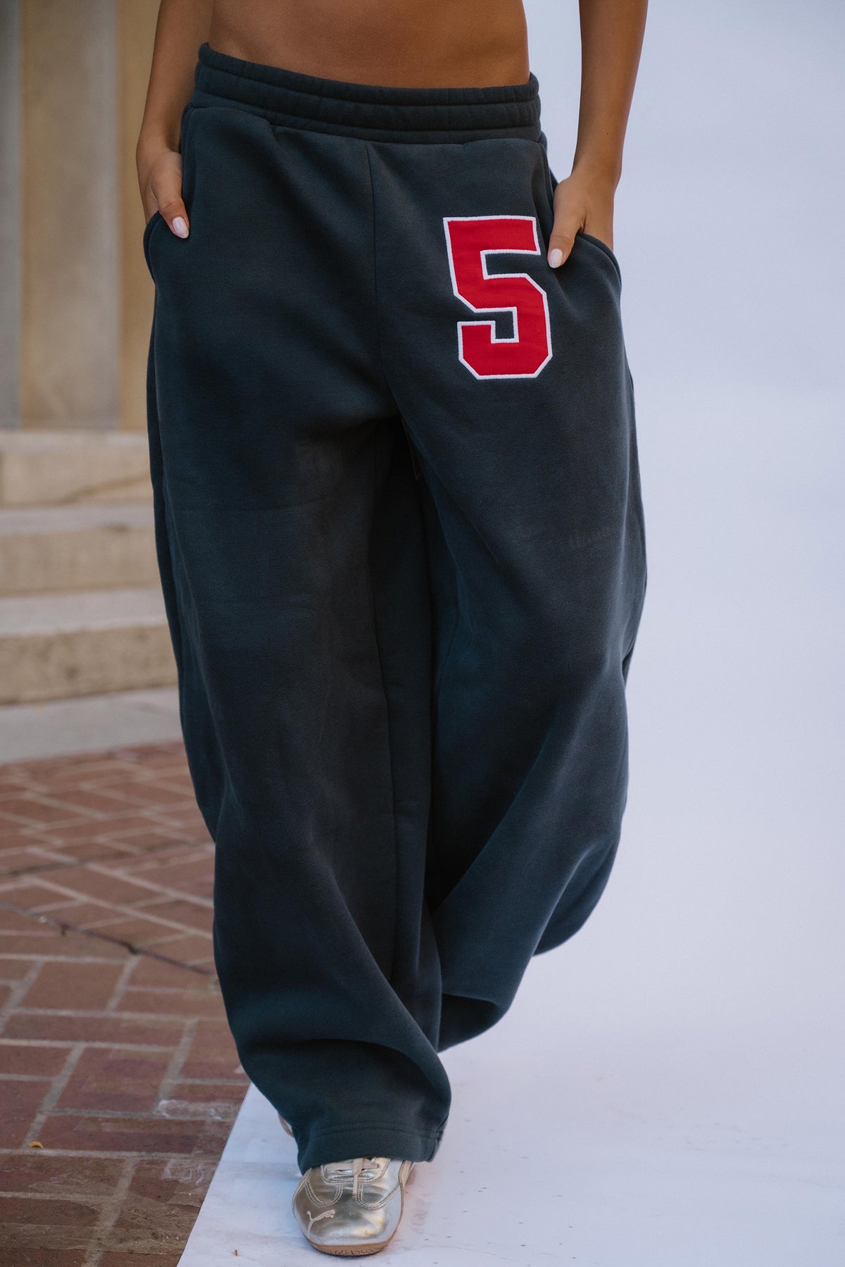 kids, navy wide-leg sweatpants with a red and white number 5 on the upper left thigh, modeled outdoors on a white surface with brick steps in the background.