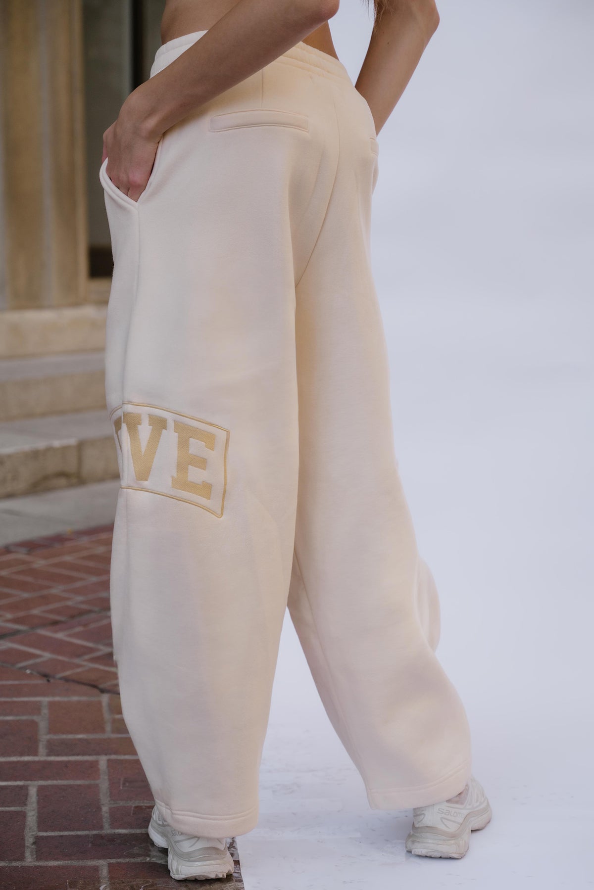 kids, A girl wearing butter yellow-colored, wide-leg sweatpants with a yellow 'FIVE' graphic embroidery on the left leg, standing outdoors on a brick sidewalk.