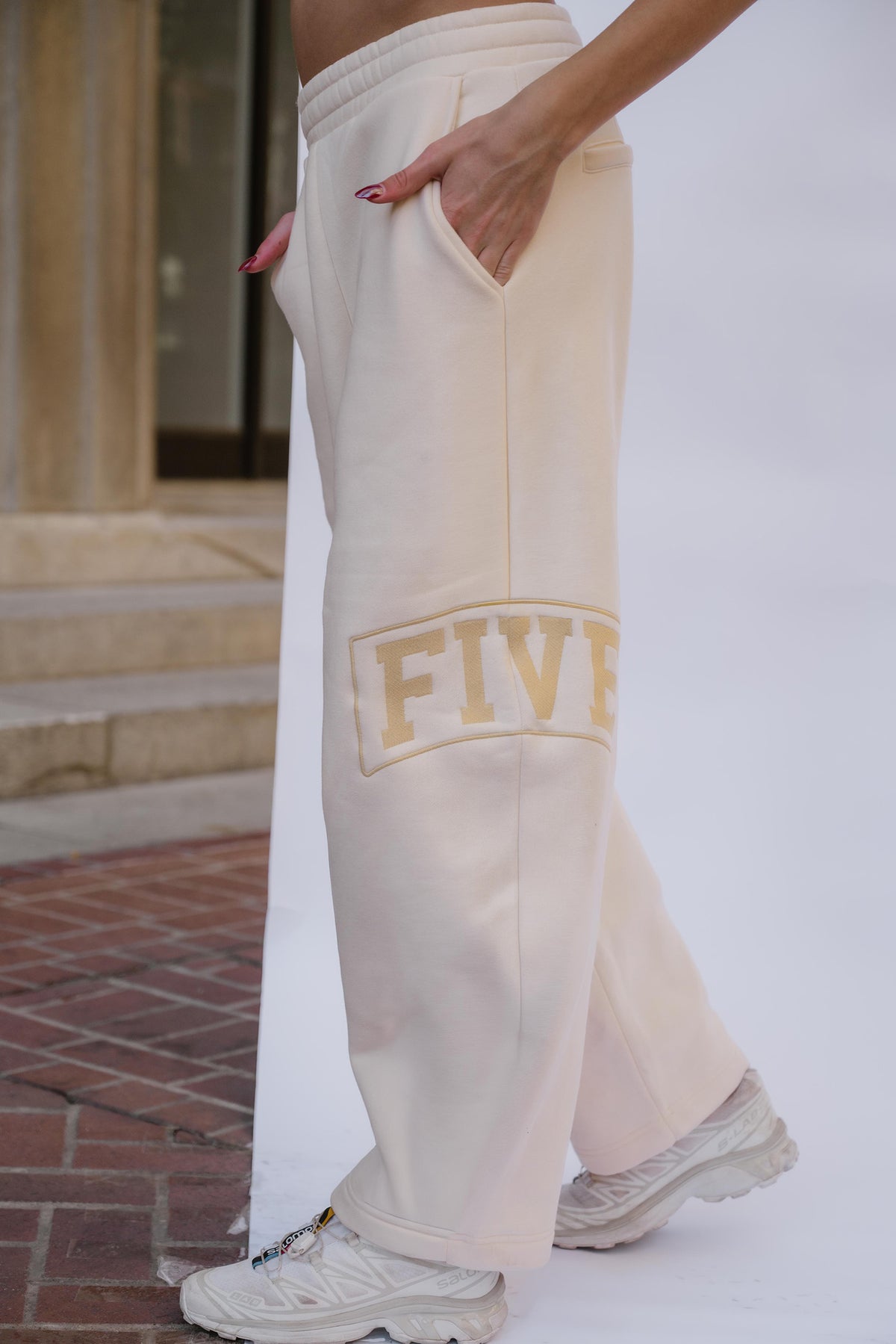 kids, A girl wearing butter yellow colored wide-leg sweatpants with a yellow embroidered 'FIVE' graphic on the leg, paired with white sneakers, standing outdoors against a white wall.
