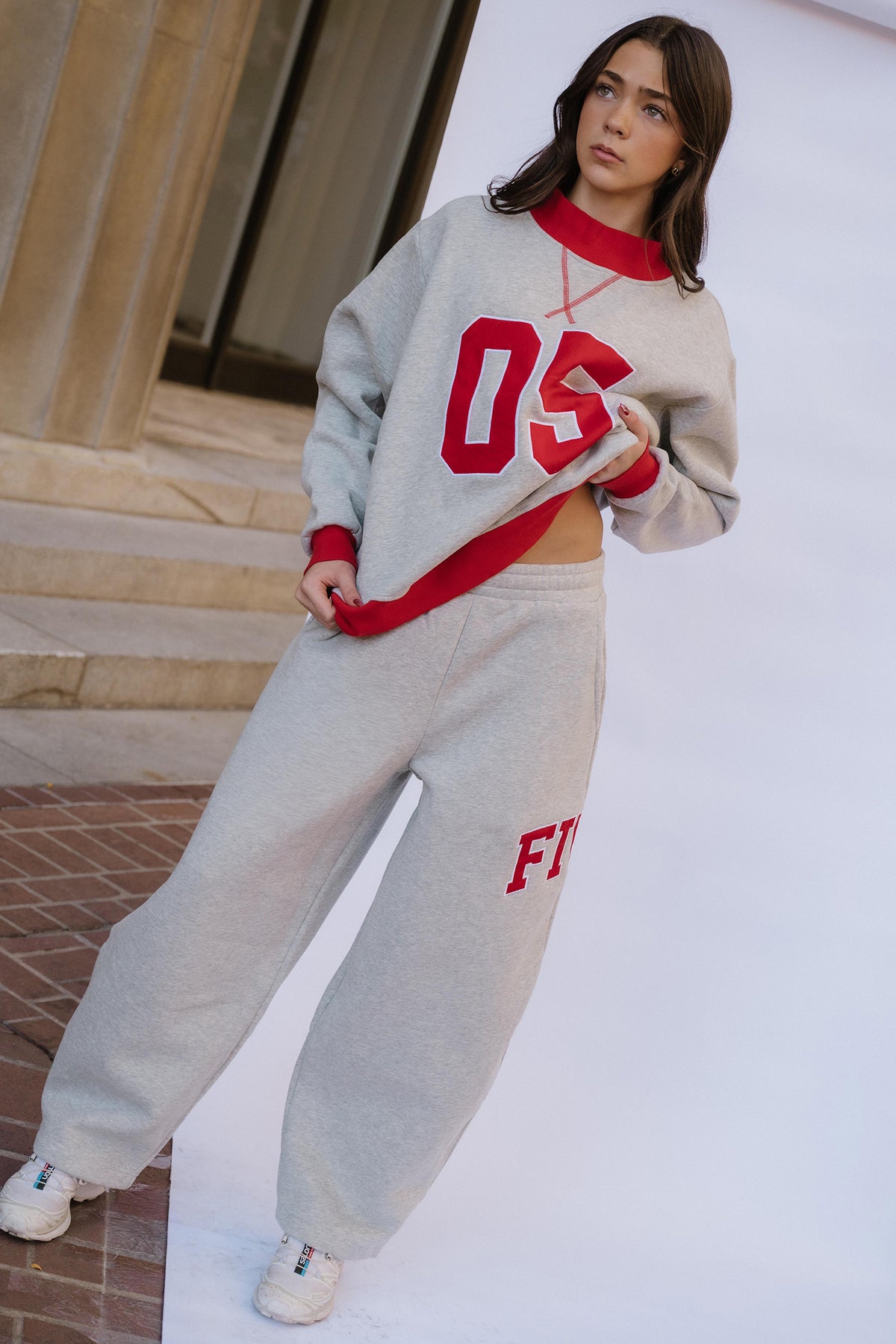 kids, A girl modeling a light gray and red two-piece sweatshirt and sweatpants set, standing outdoors against a white wall.