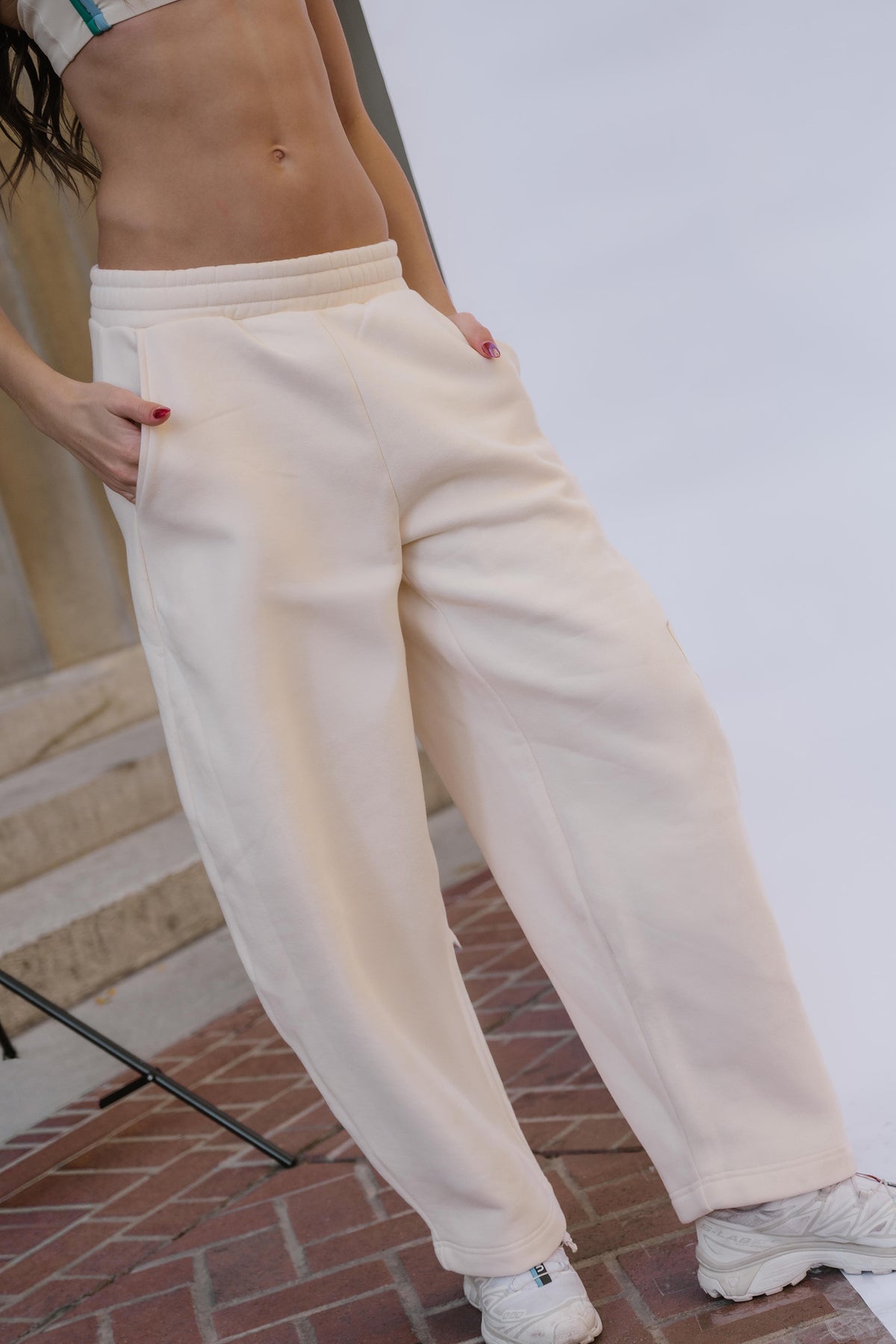 kids, A girl wearing loose, wide-leg cream sweatpants with side pockets, paired with white sneakers, standing on a brick surface against a light studio backdrop.